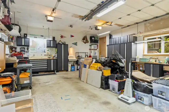 Double garage with a utility sink, lots of shelving, workshop space, great lighting and cabinetry