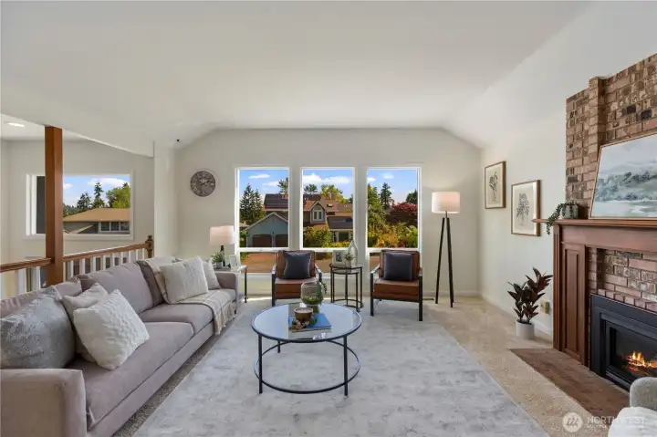 Oversized windows flood this living space with natural light and tree-lined views, anchored by a full brick fireplace with classic wood mantel.
