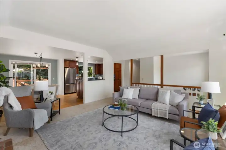 The open layout connects the living area seamlessly to the dining space and kitchen beyond, with sliding glass doors to the deck and glimpses of warm hardwood flooring.