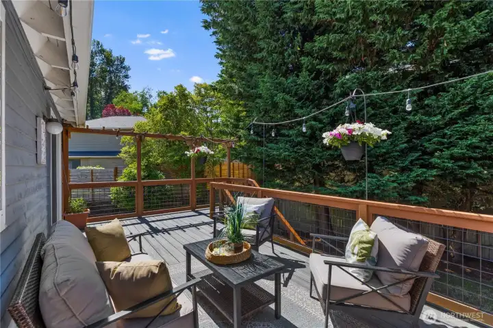 A cozy deck seating area with a pergola-style overhead structure, string lights, and treetop views offers a peaceful outdoor living space ideal for relaxing or al fresco entertaining.