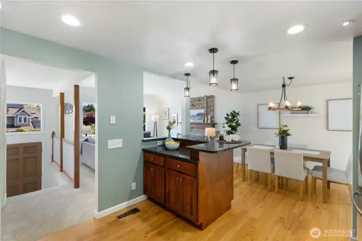 The granite-topped kitchen island anchors the space beautifully, with pendant lighting overhead and an open sightline through to the dining area, living room, and entry, showcasing the home’s impressive main-level layout.