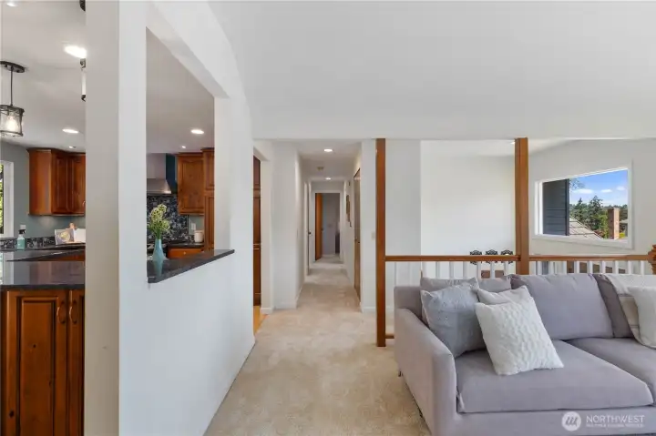 A wide, carpeted hallway connects the living area to the bedroom wing, with an open pass-through to the kitchen and views into the bright living room, demonstrating the home’s intuitive and functional layout.