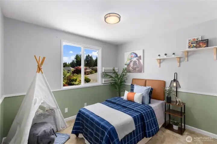 A cheerful secondary bedroom with two-tone green and white walls, a bright picture window with neighborhood views, built-in shelving, and plush carpet, a versatile space well-suited for a variety of uses.