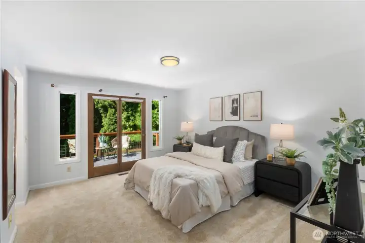 Spacious primary bedroom with plush carpet, French doors opening to a private deck, and lush green treetop views, a serene retreat with a seamless indoor-outdoor connection.