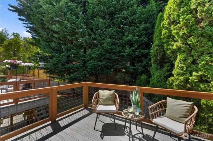 A private deck off the primary suite with composite decking, wire-panel railings, and a tranquil, tree-canopied backdrop, a quiet escape just steps from the bedroom.