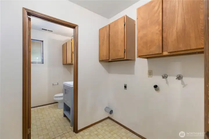 Convenient laundry area with upper storage cabinets, washer/dryer hookups, and direct access to a full bathroom,  a practical and well-positioned utility space on the lower level.