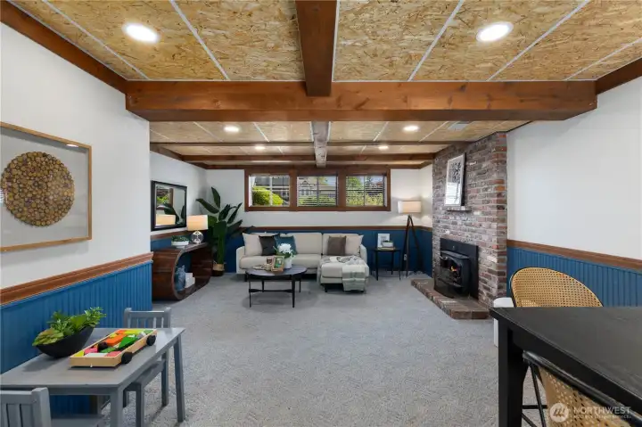 A second angle captures the full depth of this bonus space, showcasing the exposed beam ceiling, brick fireplace with insert, navy wainscoting, and abundant room for multiple seating and activity zones.