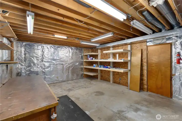A second angle of the workshop highlights built-in shelving, additional workbench space, and access to the garage, offering practical utility for any buyer needing dedicated workspace. Or finish the space to create additional living areas.
