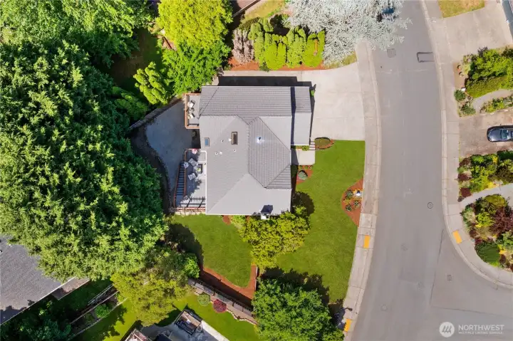Directly overhead drone shot revealing the home’s footprint, roofline layout, upper deck with pergola, fenced yard, and concrete driveway, an excellent overview of the property’s lot coverage and outdoor spaces.