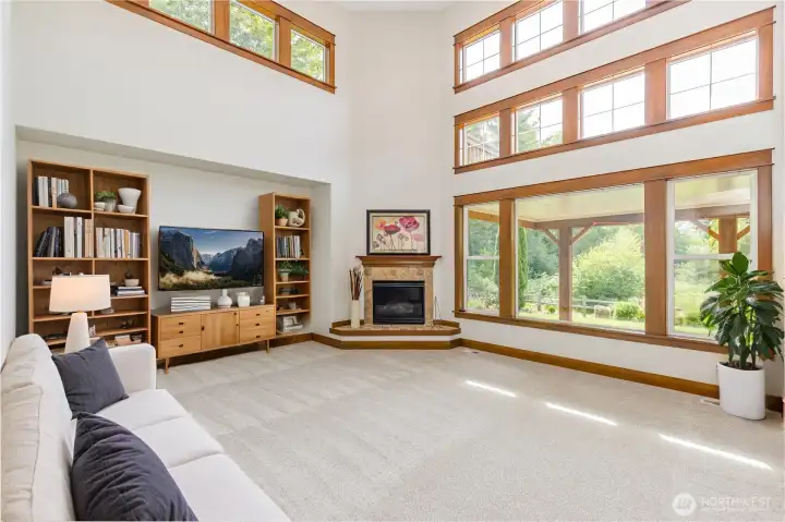 Impressive 2-story family room featuring a dramatic wall of windows that frame the natural scenery, complemented by a classic gas fireplace.