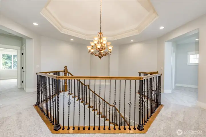 Bright and airy upper-level landing, featuring a sophisticated chandelier, elegant tray ceiling, and a refined railing that overlooks the grand foyer below.