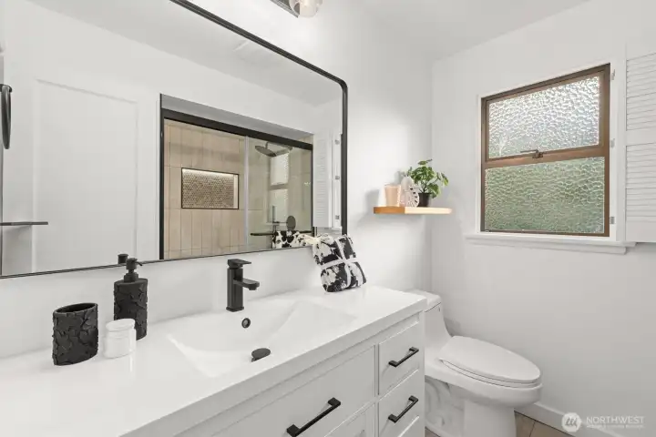 Updated 3/4 bath with new: vanity sink, floating shelf, floor to ceiling tile, penny tile, mirror, hardware, lit shower niche and lighting sconce.