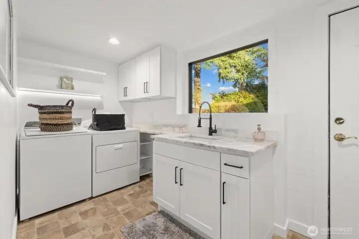 Proper laundry room with updated cabinetry, quartzite countertops, floating shelves and hardware. door leads out to backyard area.