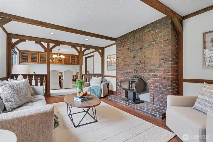 Warm main-level living area with brick fireplace and wood-burning stove, exposed beams, and open flow to the dining room.