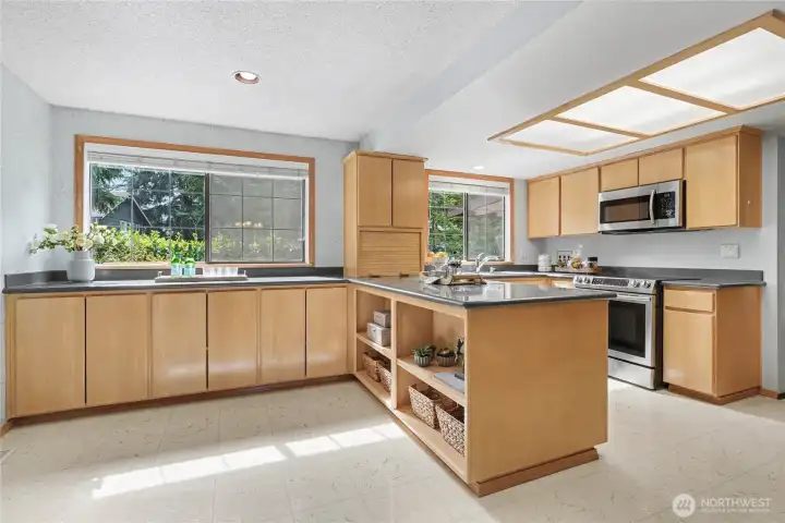Bright, spacious kitchen with abundant cabinetry, large windows, tile flooring, and a functional island with open shelving.