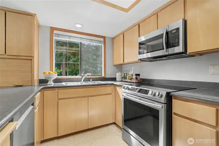 Kitchen workspace with stainless appliances, generous counter space, and a wide window offering views of the private backyard.
