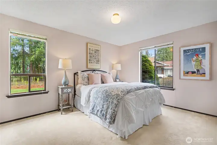 Bright secondary bedroom with large windows, soft wall tones, and views of the surrounding greenery.