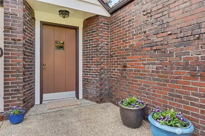 Inviting brick entryway with covered porch, updated exterior lighting, and established plantings framing the front door.