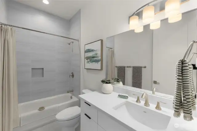Secondary bath features ceramic tile, white quartz vanity and a tub.