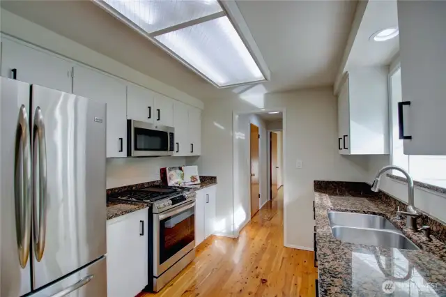 Kitchen with stainless appliances, hardwood floor, looking towards hall to laundry, den/office and garage on the left.