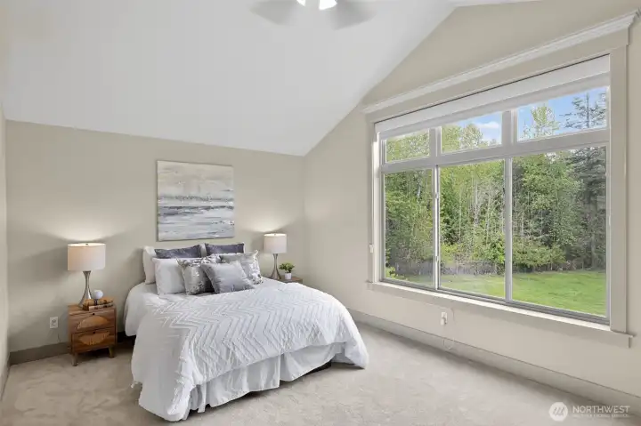 Serene primary suite with soaring vaulted ceiling & expansive window framing backyard garden views.
