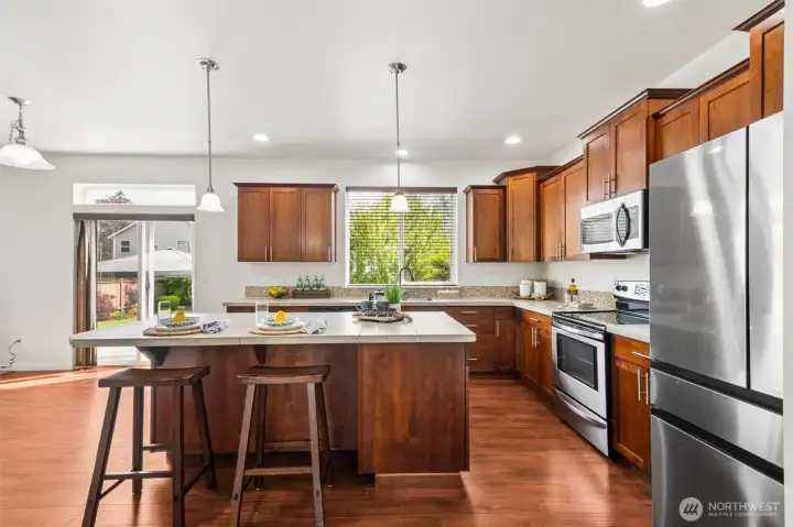 Beautiful kitchen with rich cabinetry, tile countertops, stainless appliances, and spacious center island