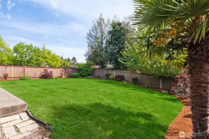 Large fully fenced backyard with lush lawn, mature landscaping, and room to play, garden, or relax