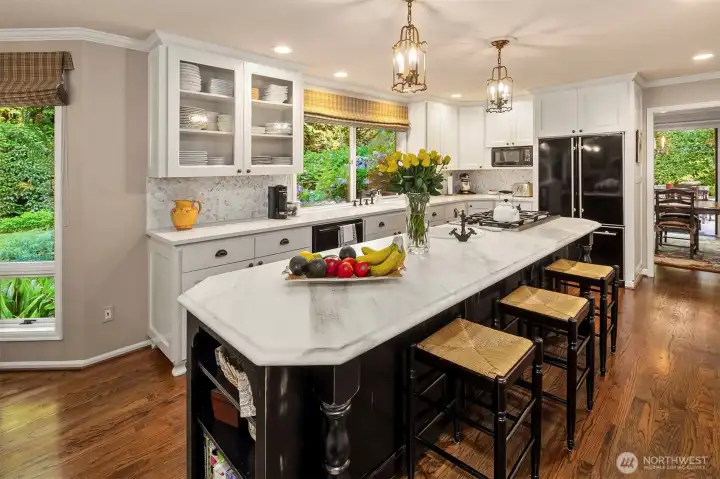 Decorative glass cabinet doors, calcutta gold marble island with prep sink, quartz countertops with herringbone marble backsplash and richly colored hardwood floors.