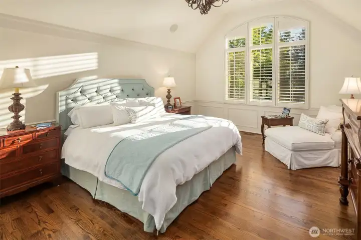 Spacious primary bedroom with hardwood floors and soaring ceiling.