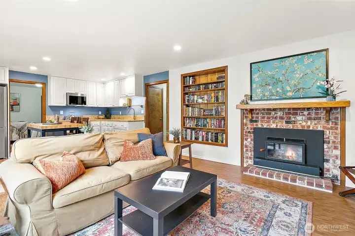 Cozy and inviting, this living area features a charming brick fireplace, custom built-in bookcase, and seamless flow to the full kitchen and dining space—perfect for relaxing evenings or hosting guests in comfort and style.