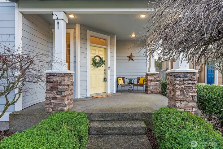 Spacious front porch with entry leading up to lined with manicured hedges