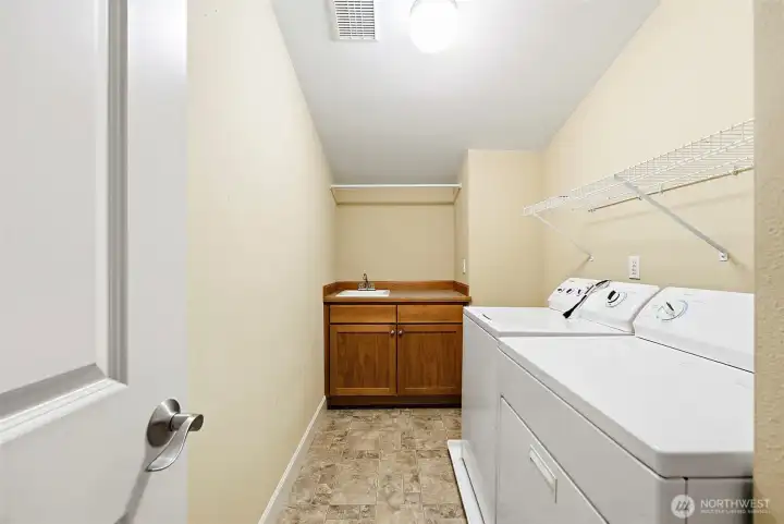 Upstairs laundry room with utility sink and storage cabinet. Wire shelve over washer and dryer unit.