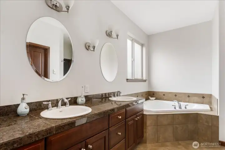Large double vanity sink with quartz tile countertops, twin mirrors, and a very large soaking tub, with tile floors & surround.