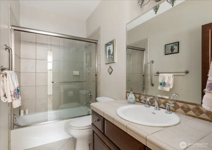 Full bath on the main level, which is adjacent to the 2nd bedroom, has a tile vanity & floor with a large shower & glass doors.