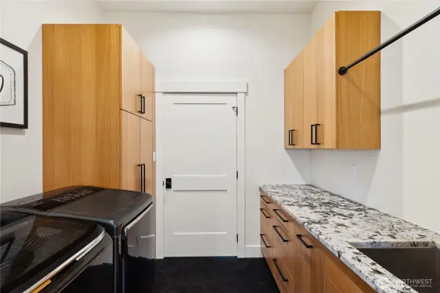 Utility room is accessed either through the primary closet or from the hallway off the kitchen area. It offers tile flooring, quality custom cabinetry, alpine white granite and utility sink.