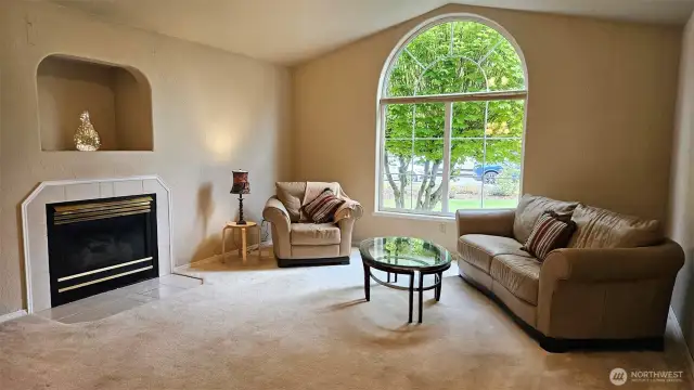 Living room with fireplace, inset niche, vaulted ceiling, ceiling fan, and large window