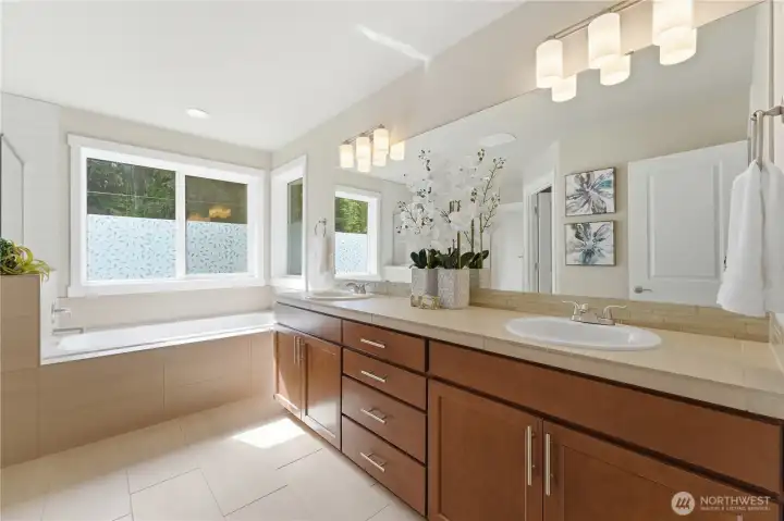 Spacious primary bathroom with double sinks, cherry cabinetry, and abundant storage, filled with natural daylight and featuring a striking separate bathtub and walk-in shower.