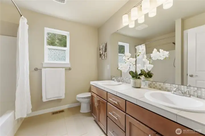 A bright upstairs full bath featuring a double vanity, generous storage, and a fresh, well-kept bath/shower combo.