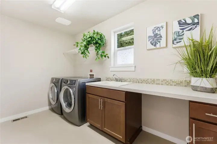 A spacious laundry and utility room with cabinetry, a convenient sink, and newer washer and dryer - a bright, practical workspace.