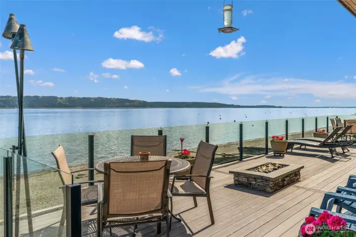 Panoramic views set the stage from this expansive no-bank waterfront deck, complete with glass railing, fire feature, and seamless access to the shoreline—perfect for relaxing, entertaining, and enjoying Camano Island’s peaceful coastal setting.