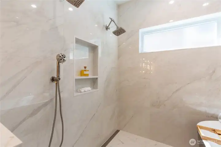 Spacious luxury shower featuring a rain shower head and handheld wand, stunning white interior, heated floors, and a massive window flooding the space with natural light.