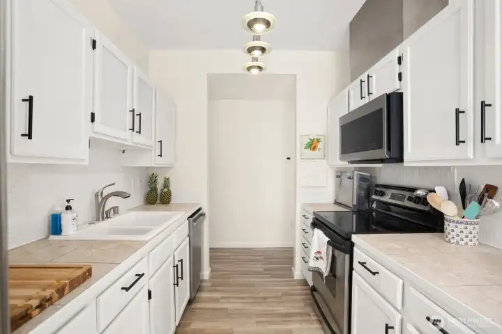 Kitchen with electric glass cooktop range, newer vented hood microwave, and ample cabinet storage facing hallway