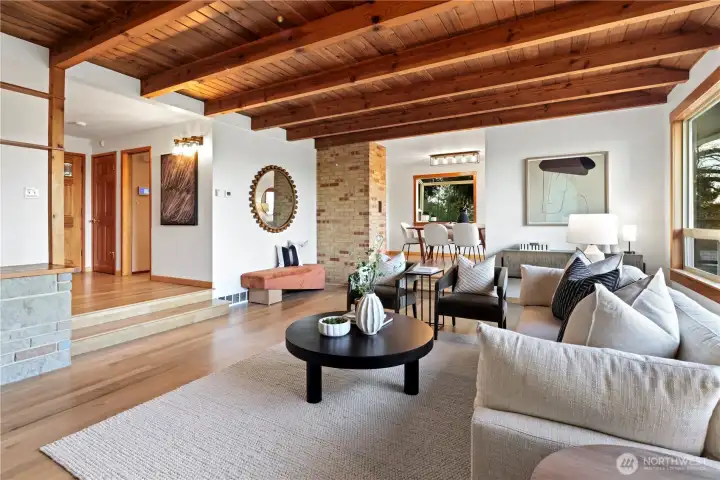Wood beams and natural shiplap ceilings add timeless architectural character. View looking back to the front entry and across to the dining room. Brand new white oak hardwood floors throughout the living room, dining room, kitchen, entry and main hallway.