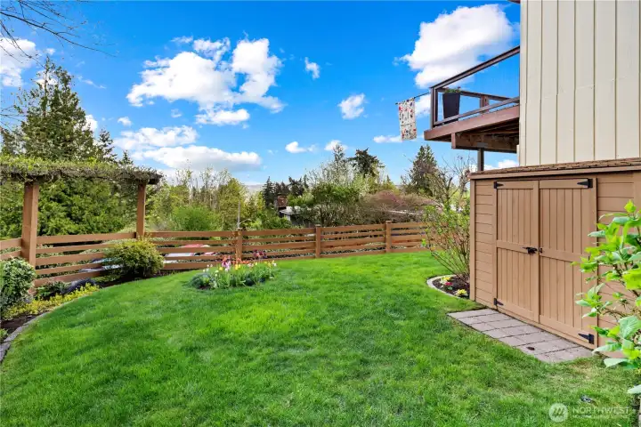 Trellis with seasonal blooms and lush landscaping create a scenic backyard retreat. Outdoor storage shed will come in handy for garden tools and lawn equipment.