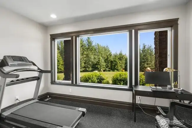 Thoughtfully designed home gym with premium rubber flooring and a statement window capturing serene backyard and wooded views. This bright, energizing space blends performance and tranquility — bringing the outdoors in while supporting your active lifestyle.