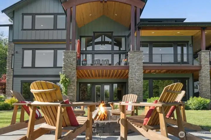 Striking timber beams, stacked stone columns, and soaring windows define this impressive rear elevation. The covered upper deck overlooks a thoughtfully designed patio with built-in firepit seating — an ideal setting for entertaining or unwinding in a private, serene setting.