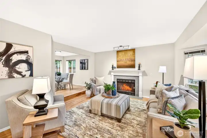 The sun-filled living room anchors the main level with warmth and comfort, featuring a beautifully appointed tile fireplace, refinished hardwood floors, and a seamless connection to the raised dining area — an inviting space designed for everyday living and effortless entertaining.