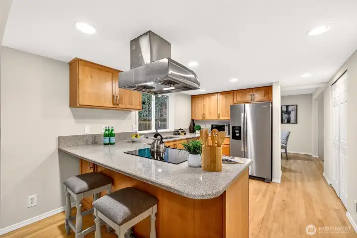 The peninsula with bar seating creates a natural hub for casual meals and conversation, while the cooktop with overhead vent hood and quartz counters bring both style and serious cooking capability to this well-appointed kitchen.