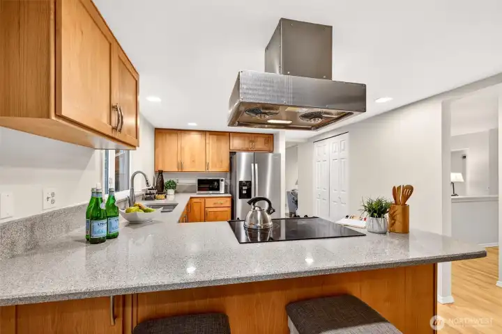 Expansive quartz countertops and a center peninsula cooktop give this kitchen a functional layout that serious cooks will appreciate, with an easy sightline through to the dining and living areas that keeps everyone connected while meals are prepared.