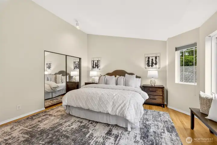 Spacious and serene, the primary bedroom offers mirrored closet doors, hardwood floors, and windows framing the treetop surroundings — a quiet sanctuary that provides both the scale and calm that a true primary suite demands.